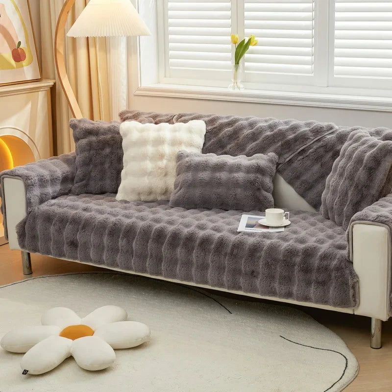 Housse de canapé en fausse fourrure gris anthracite avec des coussins contrastants en blanc crème, offrant une esthétique moderne et raffinée